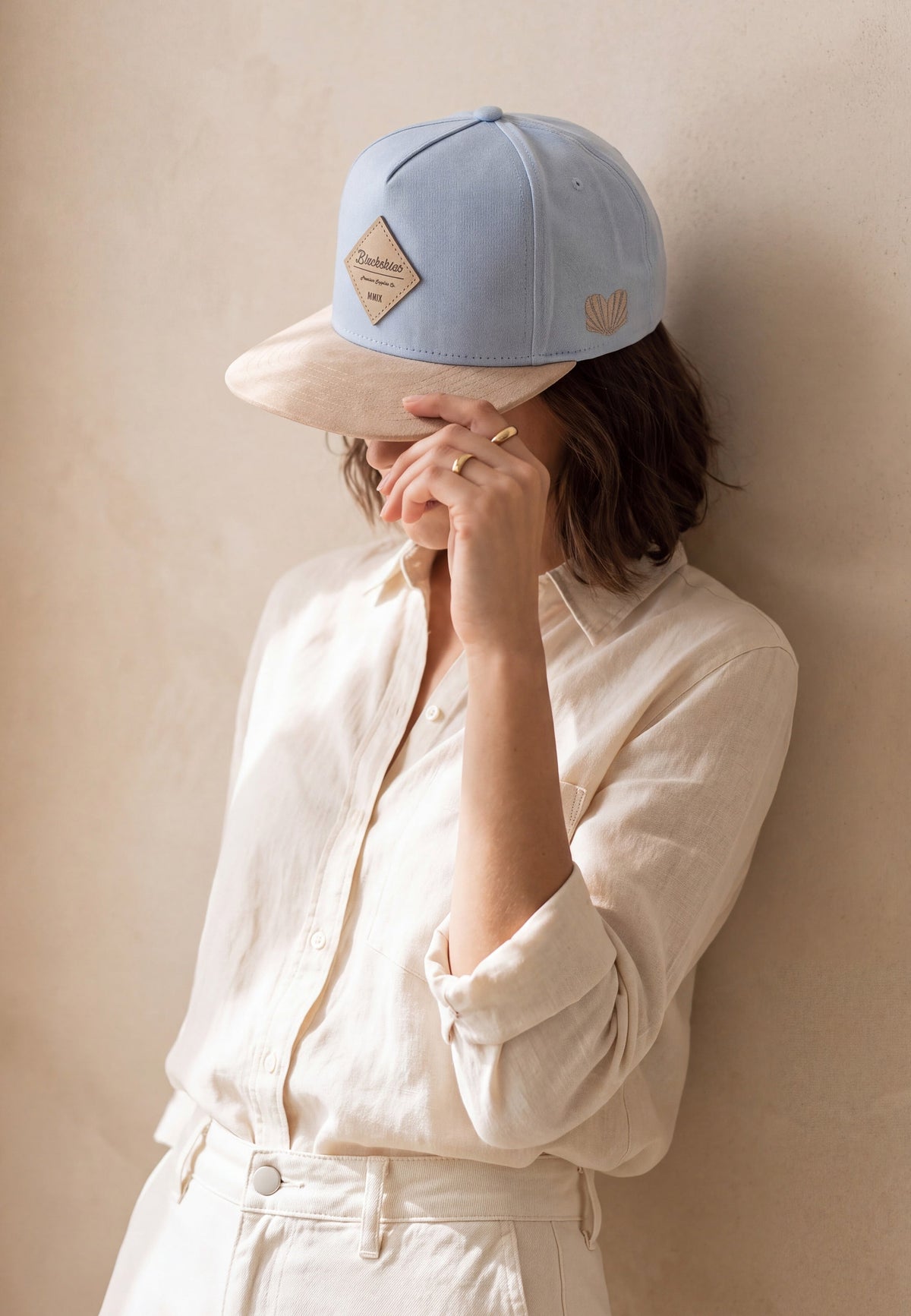 Woman wearing a light blue snapback cap from Blackskies with a pale beige suede Visor