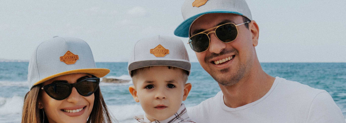 Two adults and a child wearing matching hats with a logo, standing by the ocean.