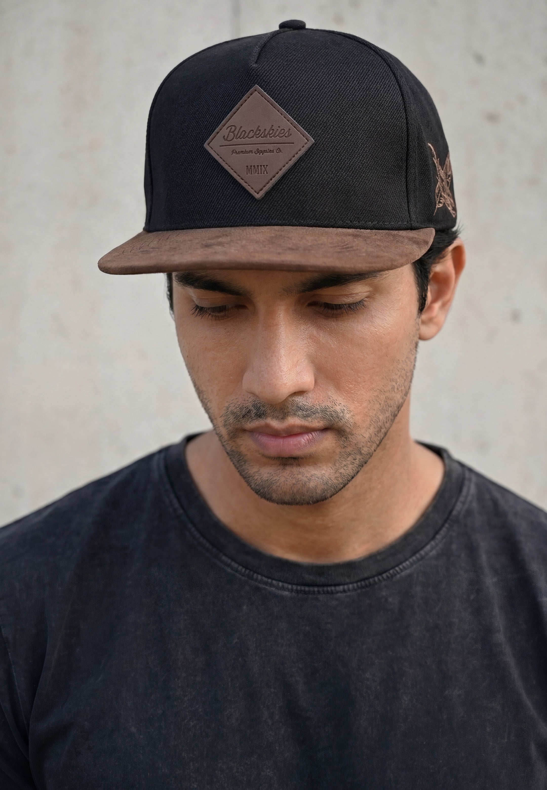 Man wearing a black and brown blackskies  snapback cap with a visible brand logo against a neutral background