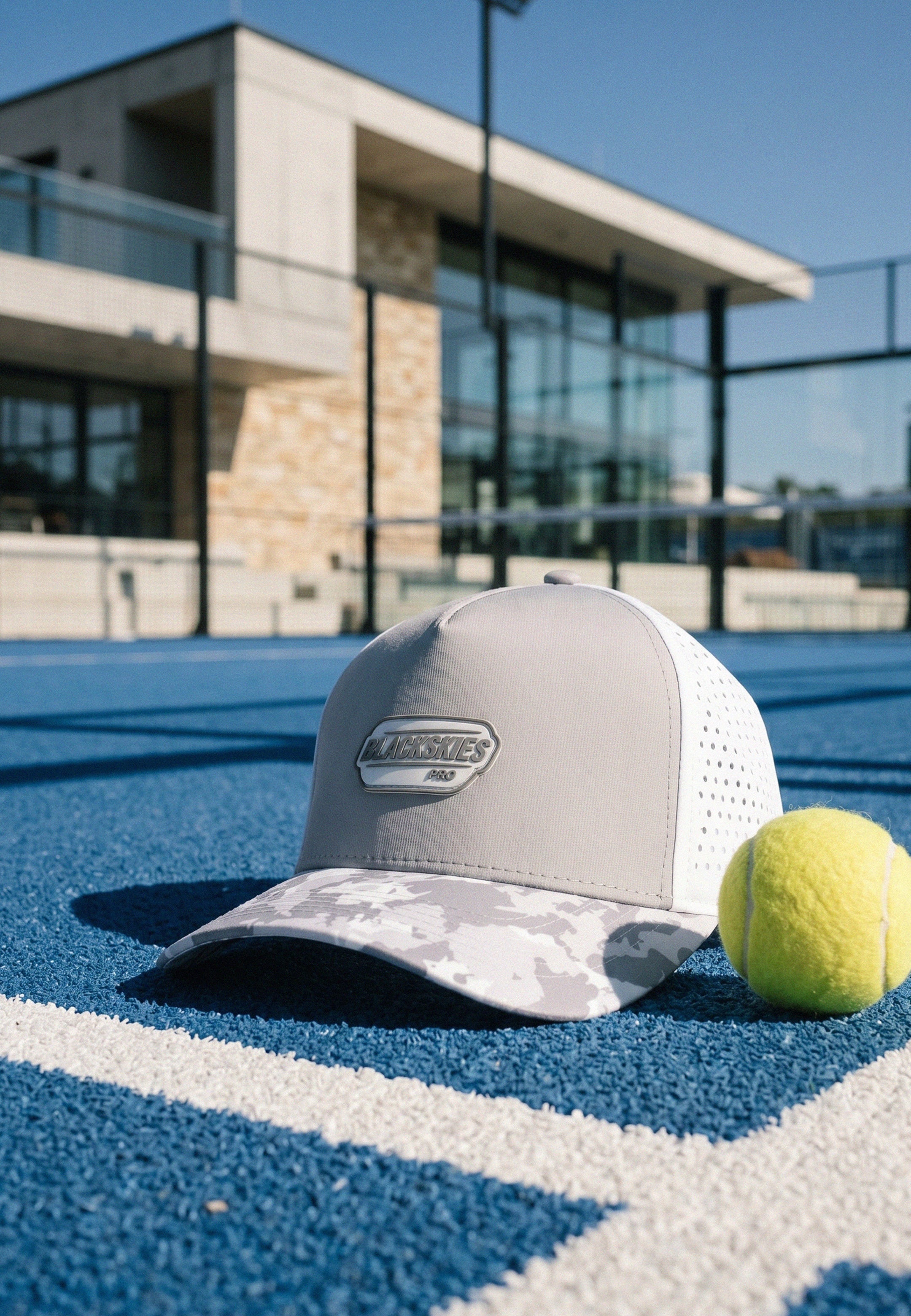 Gray cap with white mesh and a logo on a tennis court, with a tennis ball nearby.