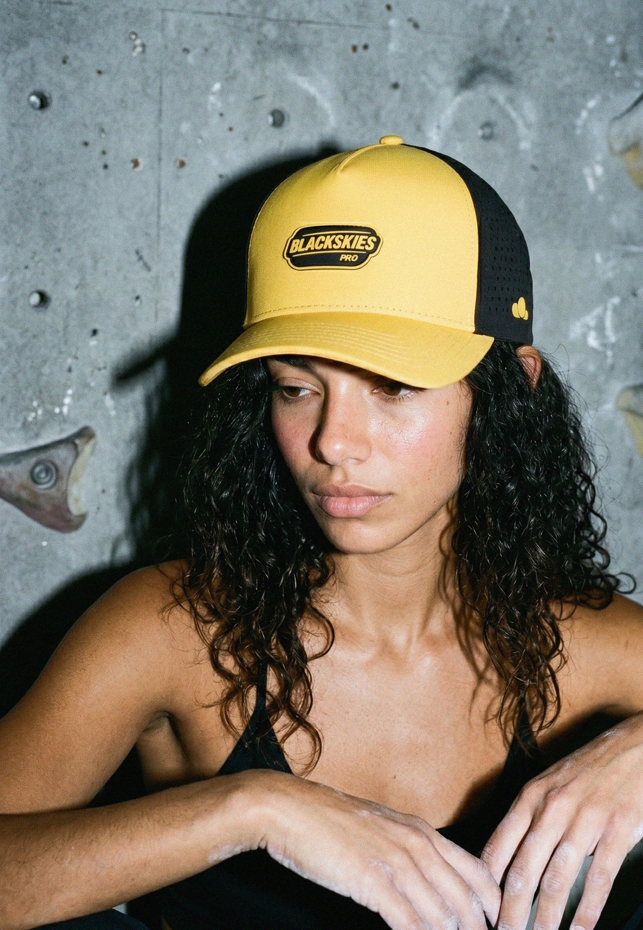 Person wearing a yellow and black cap with 'Blackskies' logo against a textured wall.