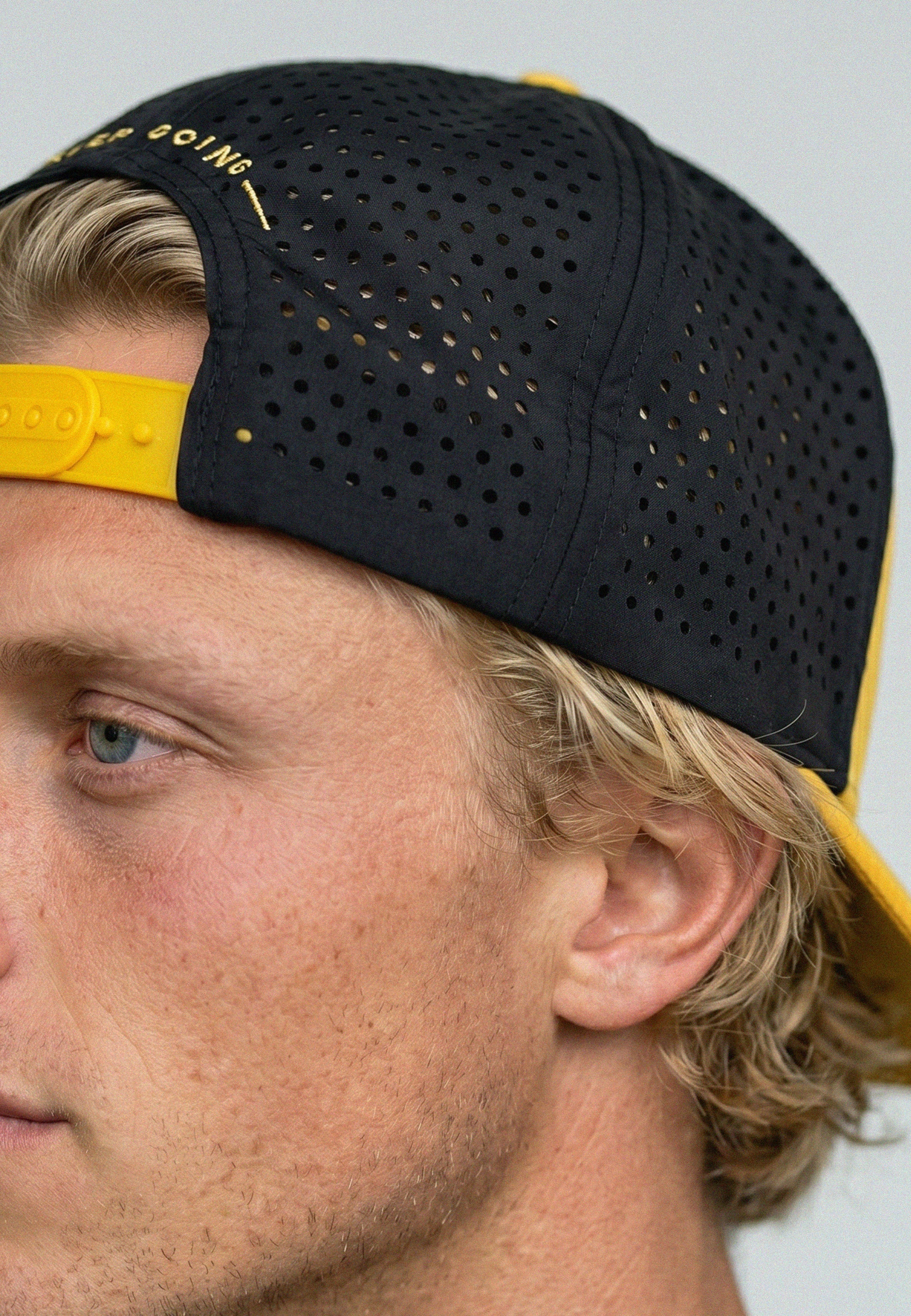 Person wearing a black and yellow cap with visible branding on a neutral background