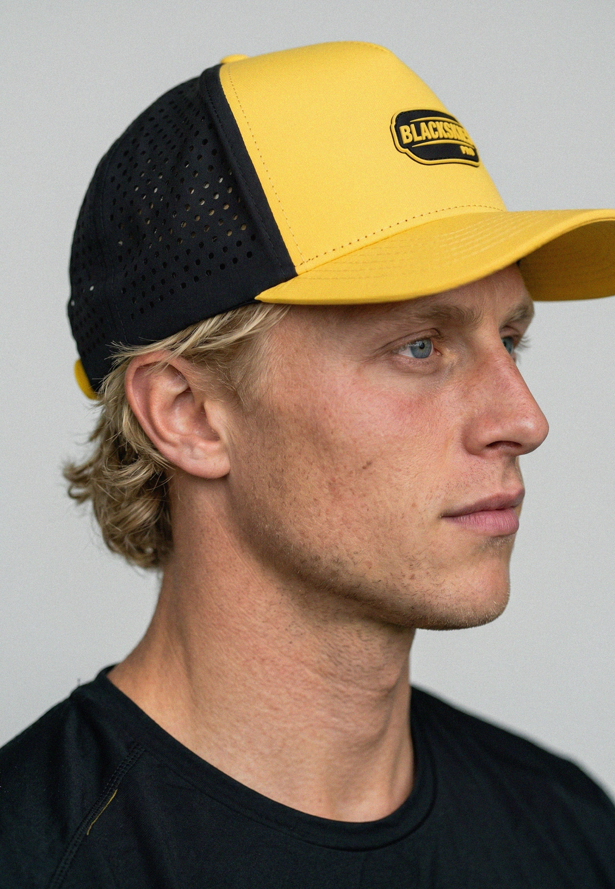 Man wearing a black and yellow cap with a brand logo on a gray background
