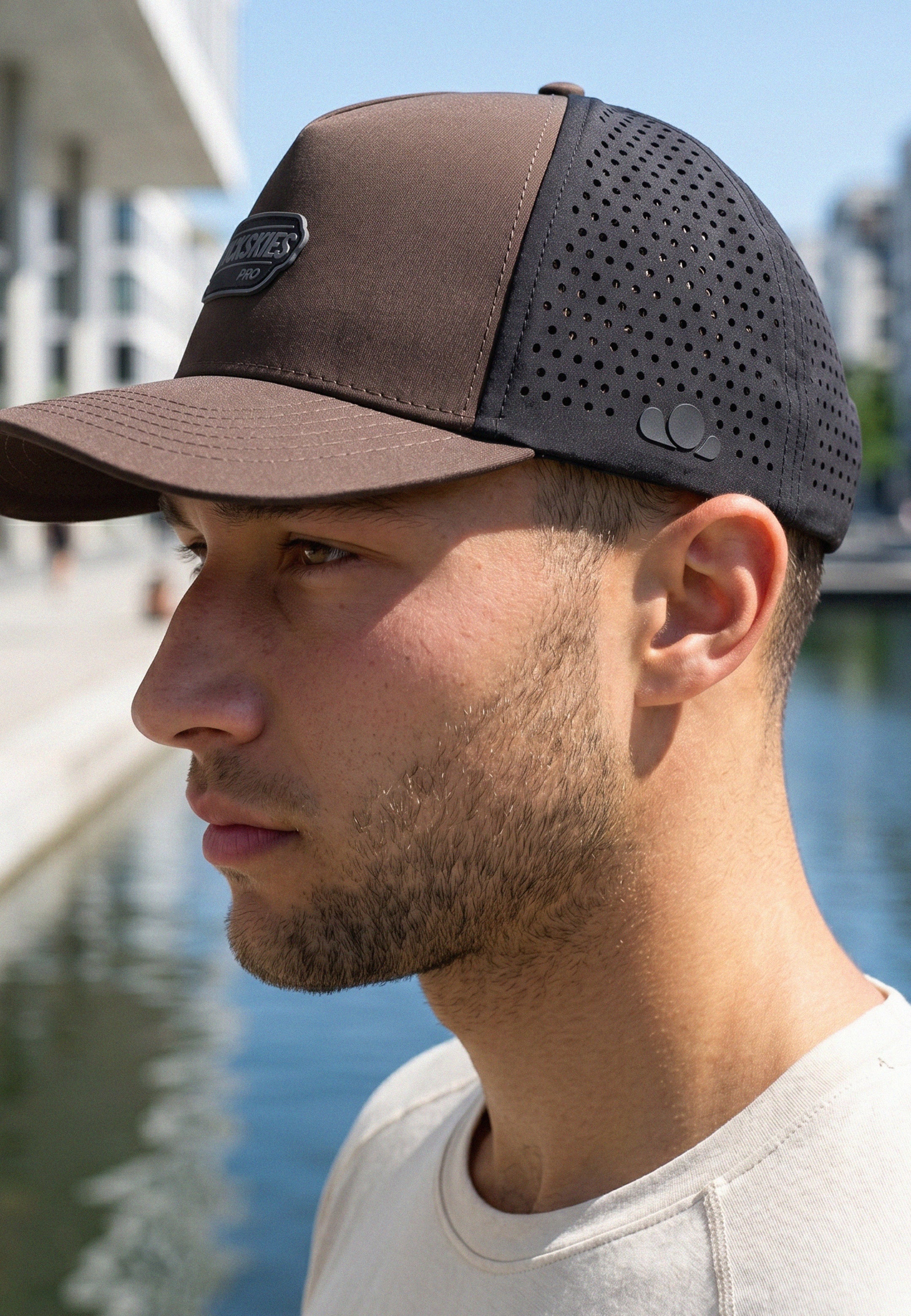 Man wearing a brown and black baseball cap by a waterfront.