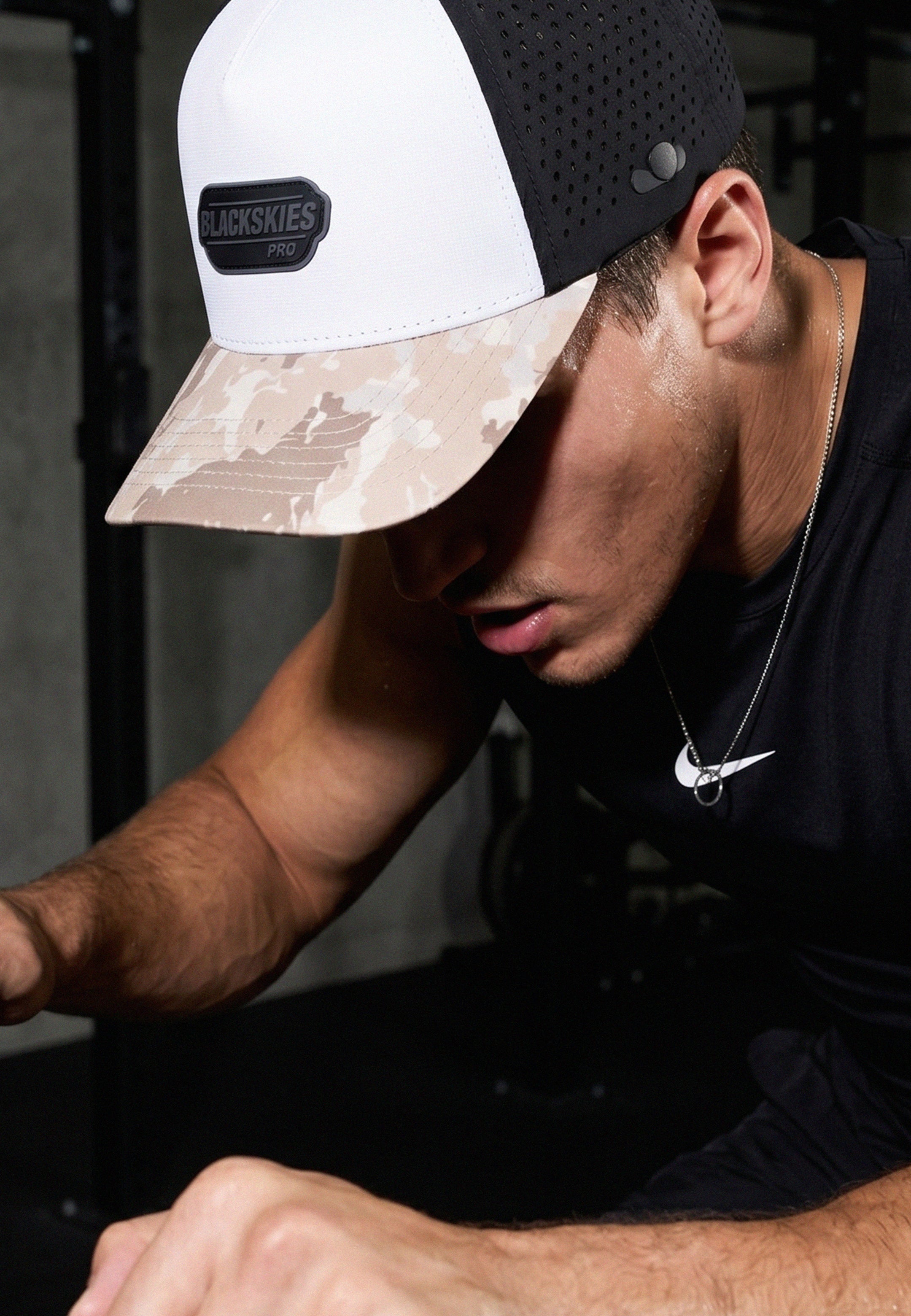 Person wearing a camouflage and black cap with a visible brand logo.