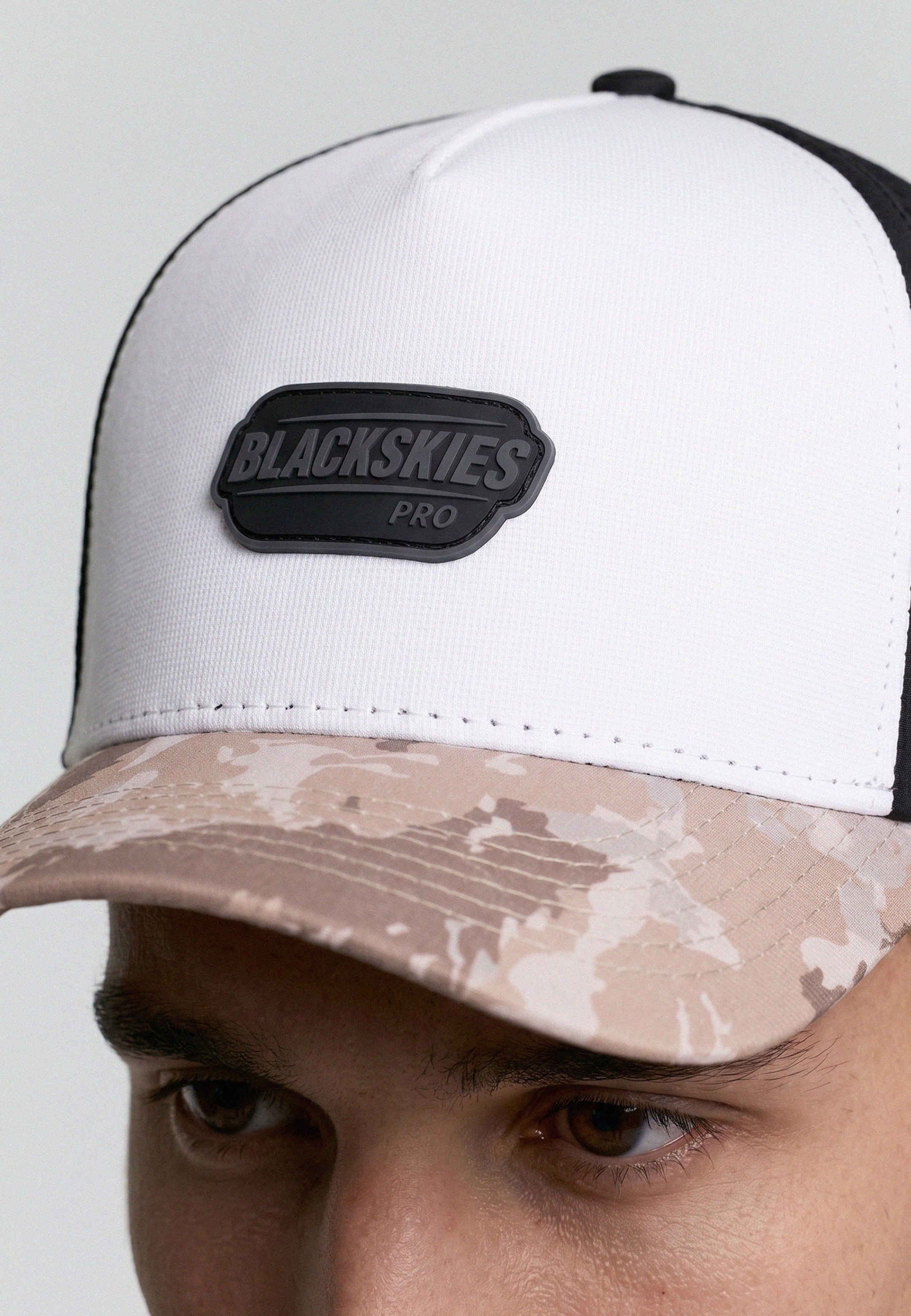 White cap with camouflage brim and 'BLACKSKIES' logo on a plain background