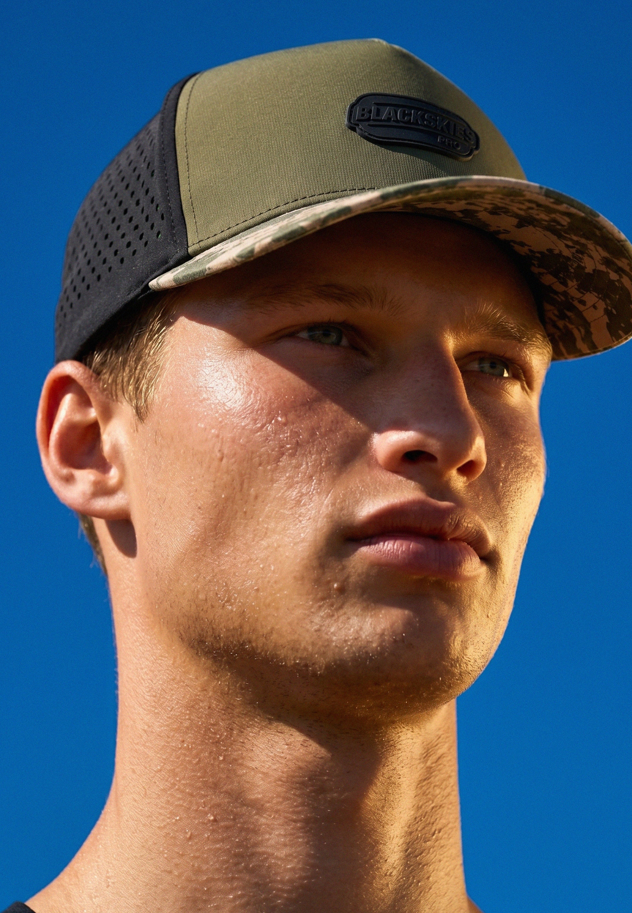 Close-up of a person wearing a green and black cap against a blue sky.