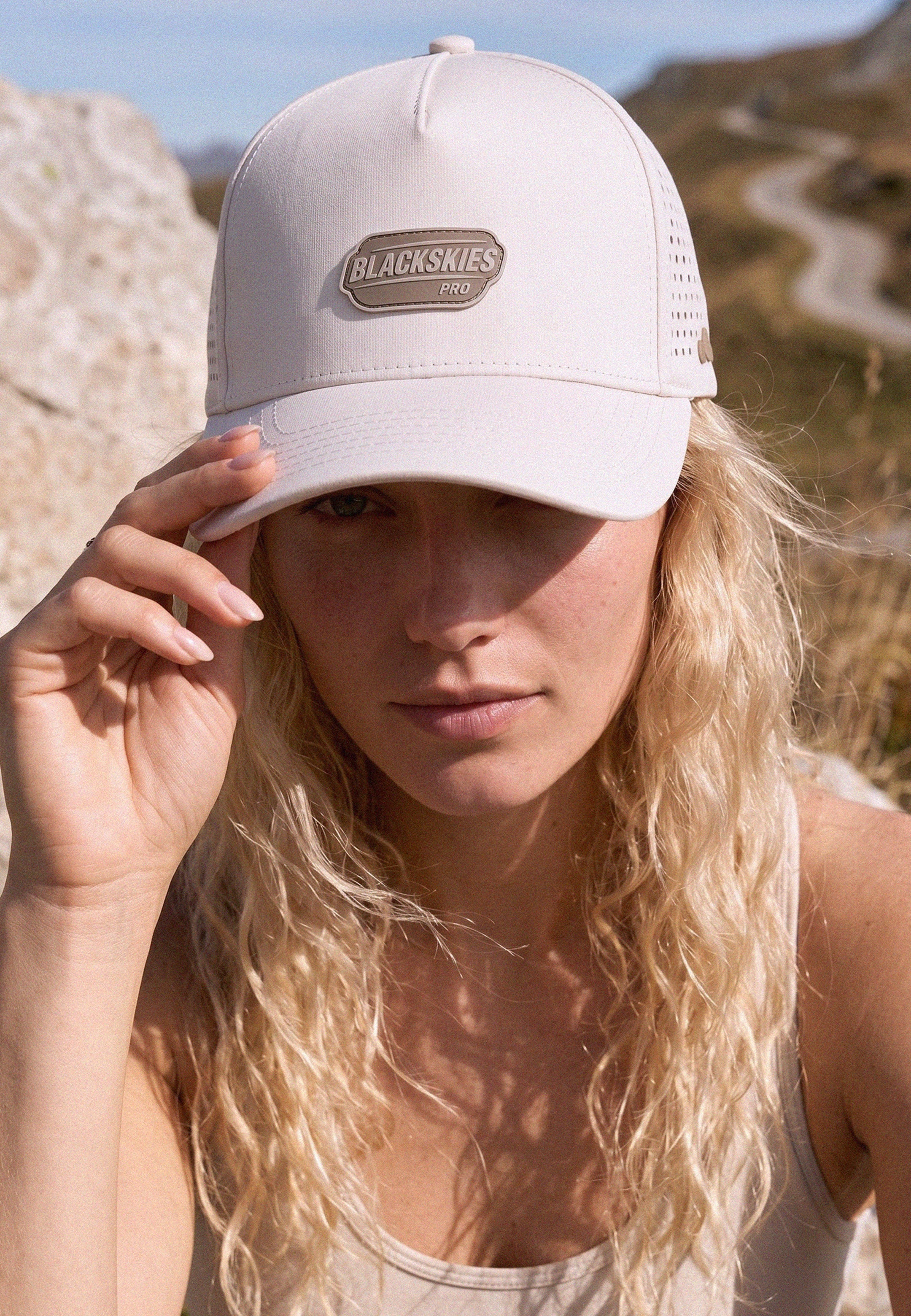 Woman wearing a beige cap with 'Blackskies' logo against a natural background