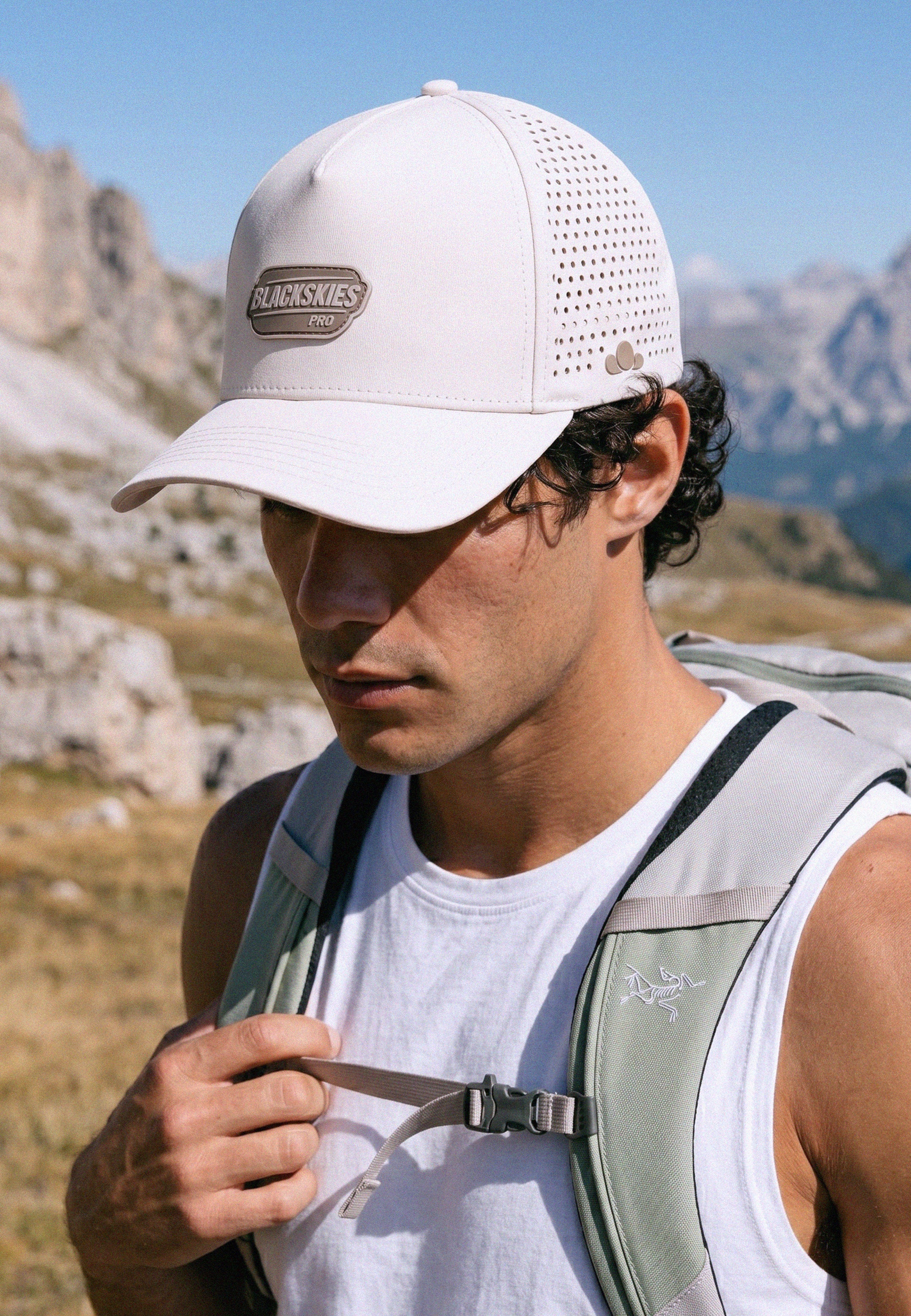 Man wearing a cap and hiking backpack with mountains in the background