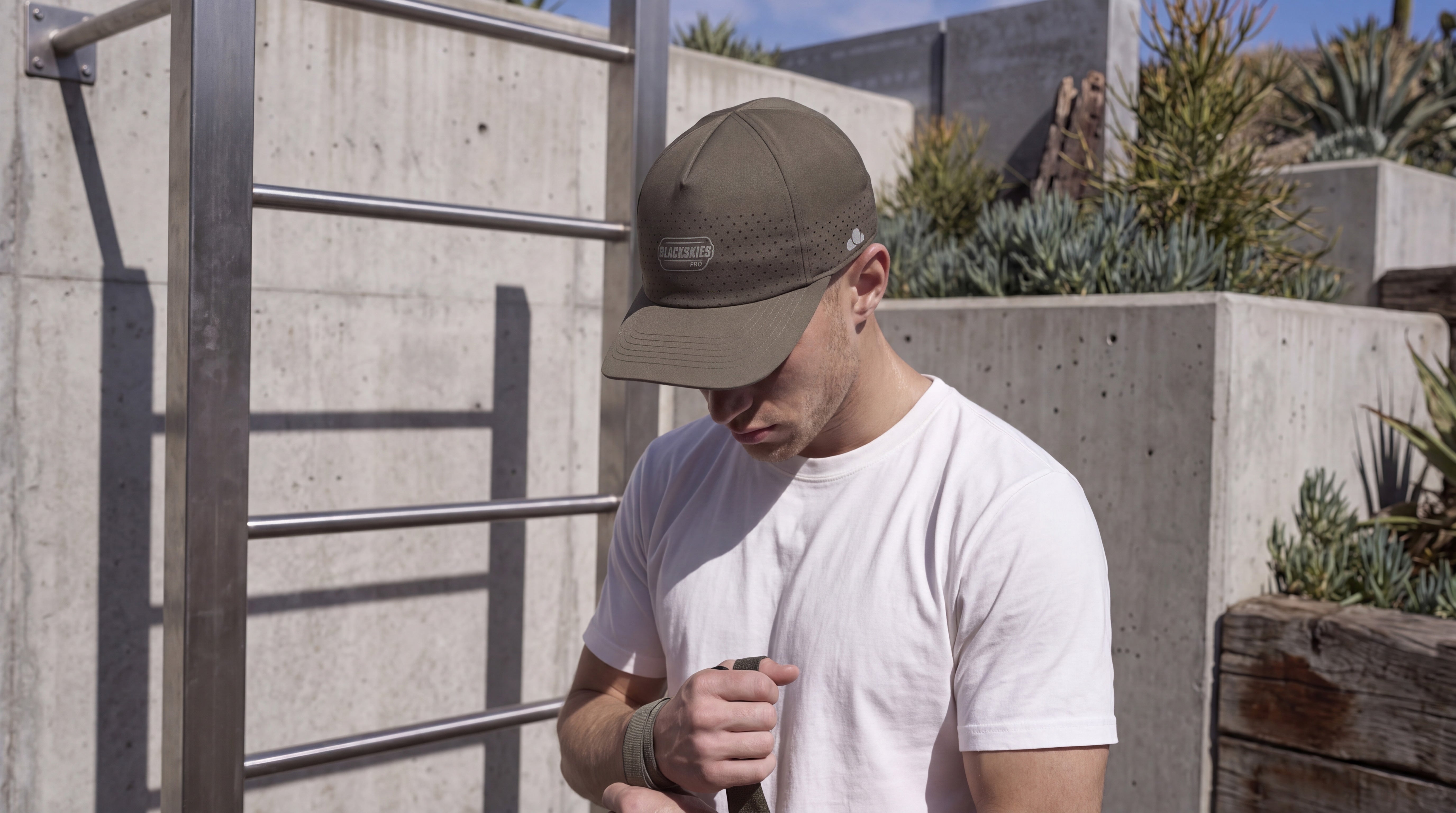 A man wearing an olive green sport performance baseball cap and a white t-shirt, working out outdoors.