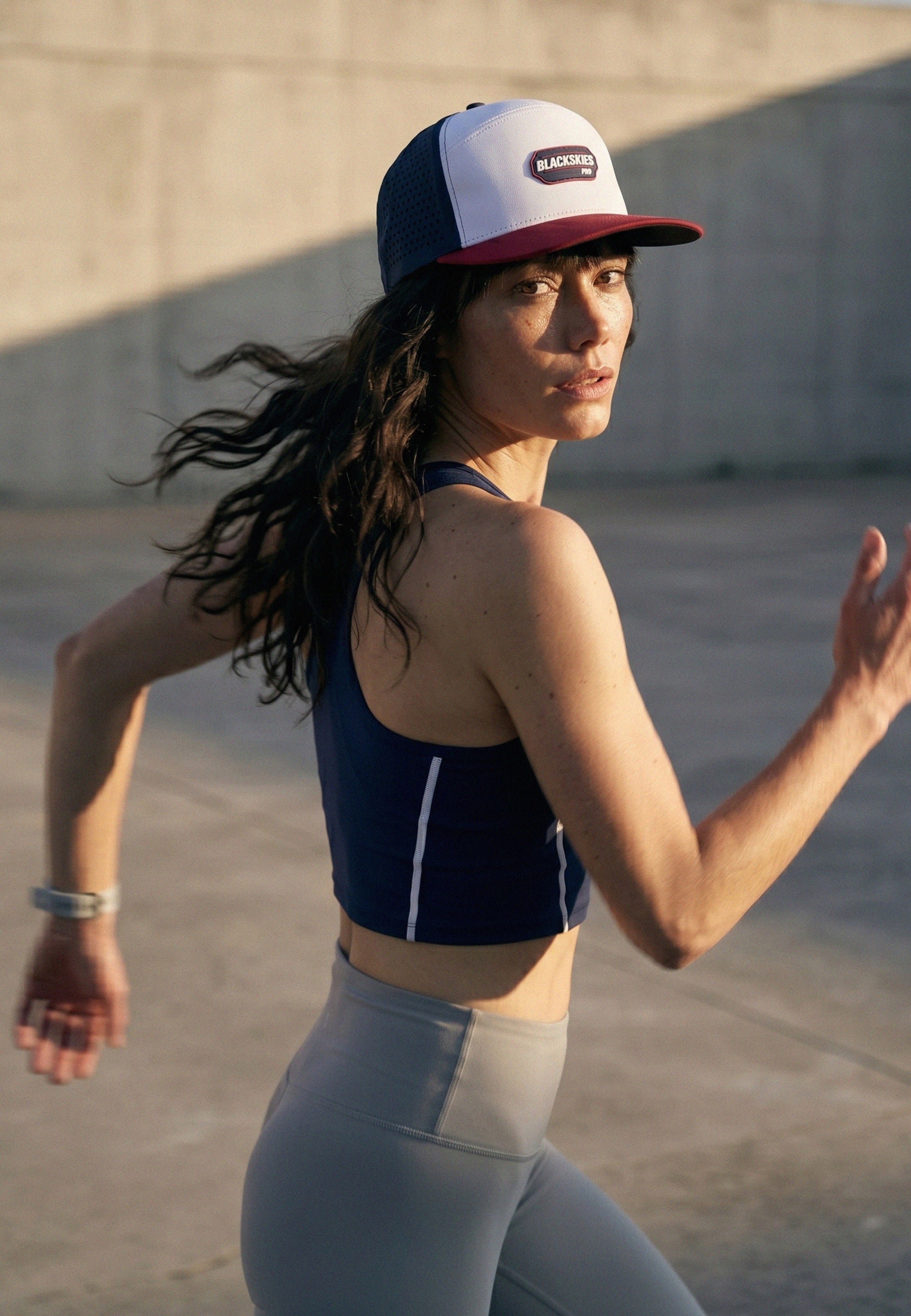 Woman running outdoors wearing a performance sport cap from blackskies and athletic wear.