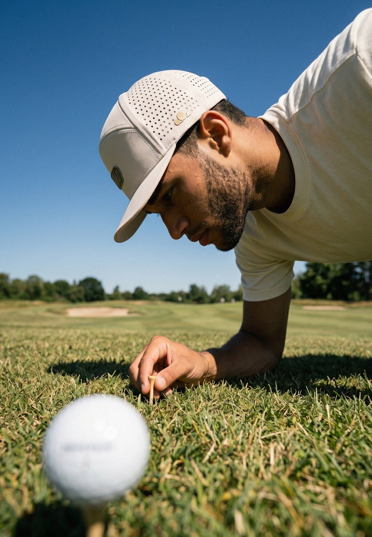 Man preparing to putt a golf ball on a green golf course with a clear blue sky.