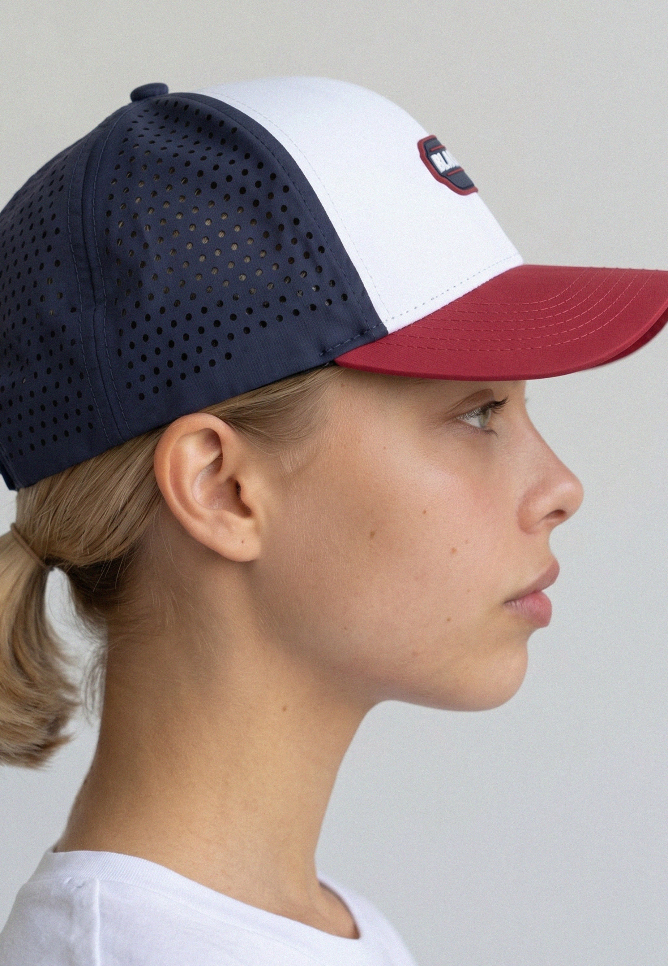 Person wearing a navy and white baseball cap with a red brim on a plain background