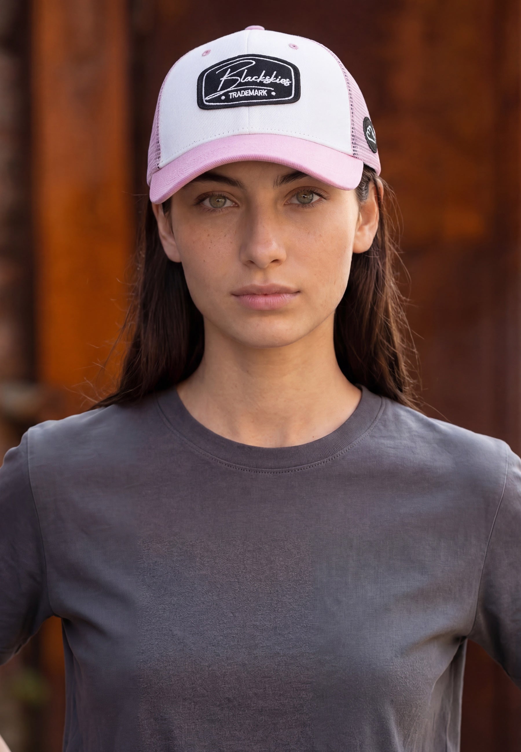Woman wearing a pink blackskies baseball trucker cap with a logo against a blurred background