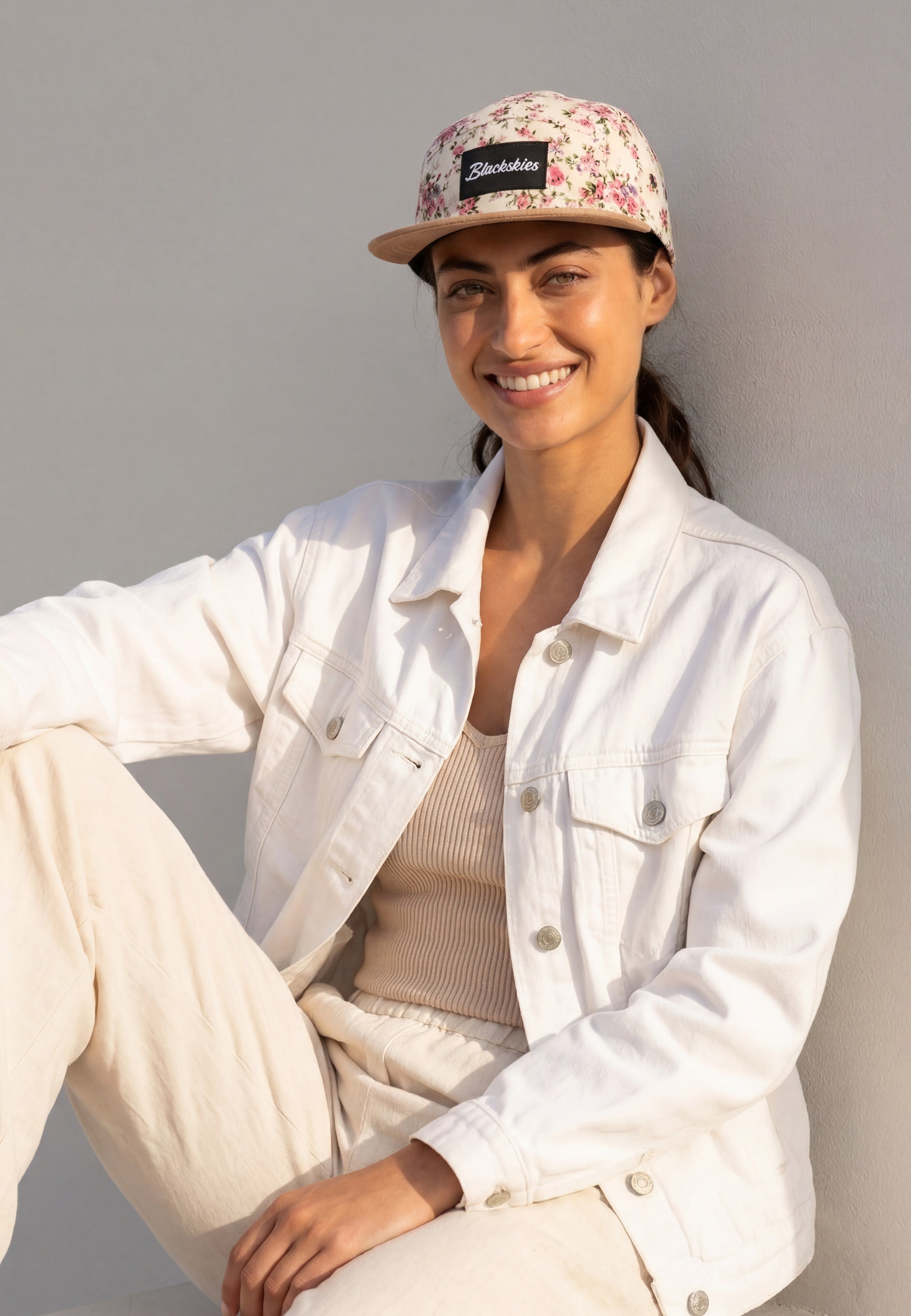 Woman wearing a white jacket and floral cap against a gray background