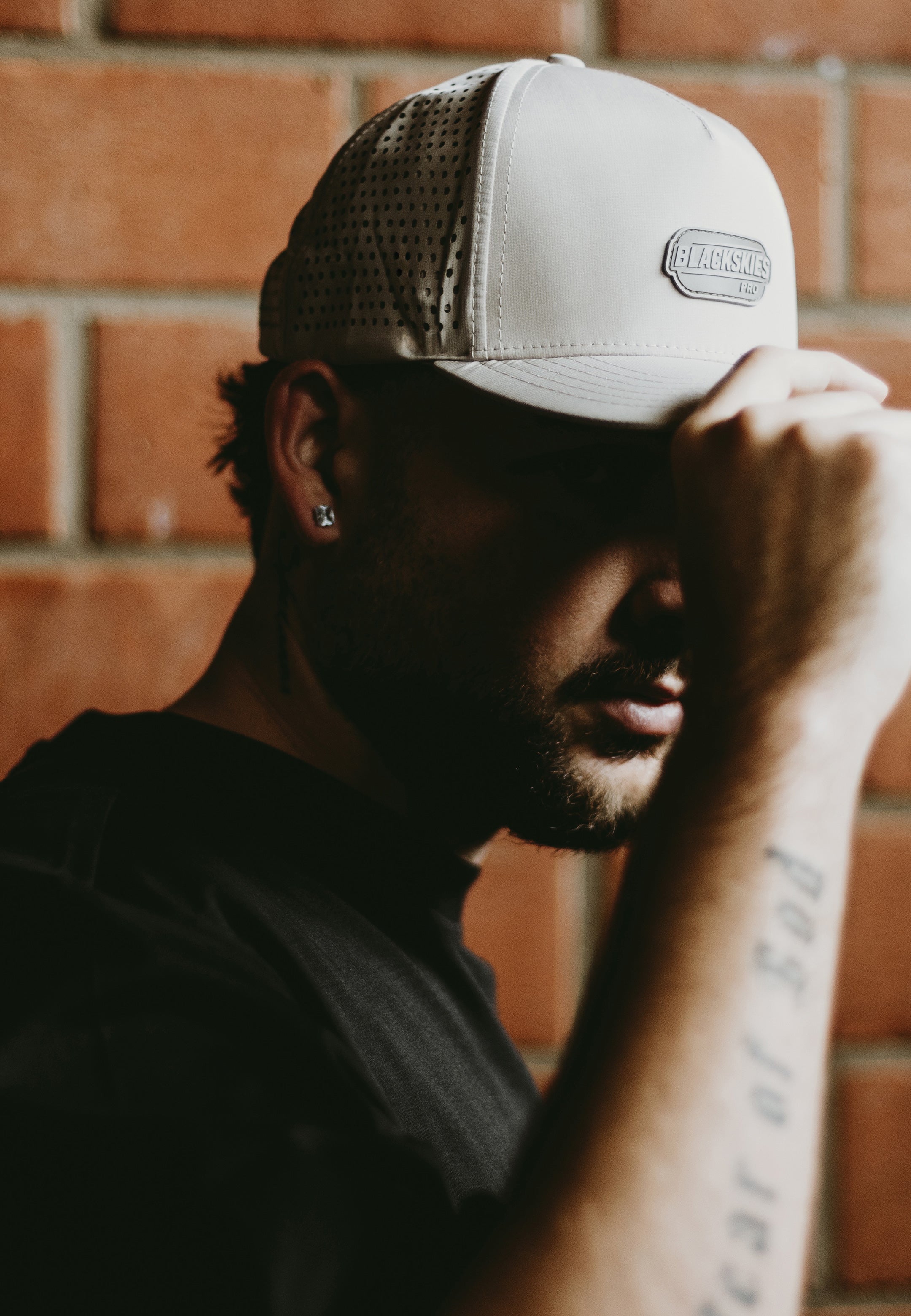 Man wearing a sport performance cap with a blackskies brand logo against a brick wall